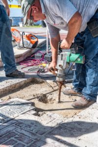Man jackhammers concrete near fountain and sculpture.